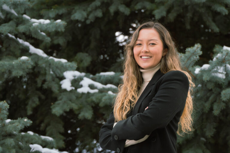 Julia Bicknell poses against pine tree with snow on it