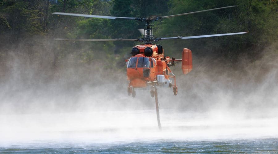 Firefighting-helicopter-is-hovering-over-body-of-water-to-refills-water-tanks