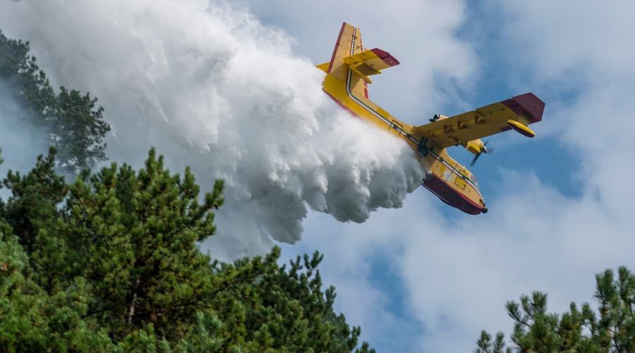 Yellow Water Bomber Aircraft Dropping a Large Volume of Fire Suppressant on Forest Fire
