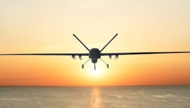 Unmanned military drone patrols the territory at sunset, flying above water surface. The view is straight ahead